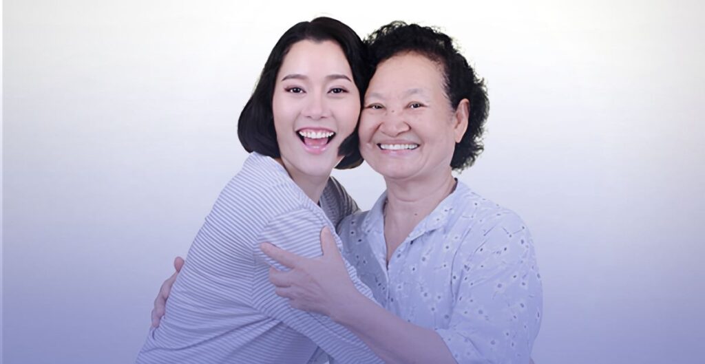 Two women smiling and hugging happily against a light background.