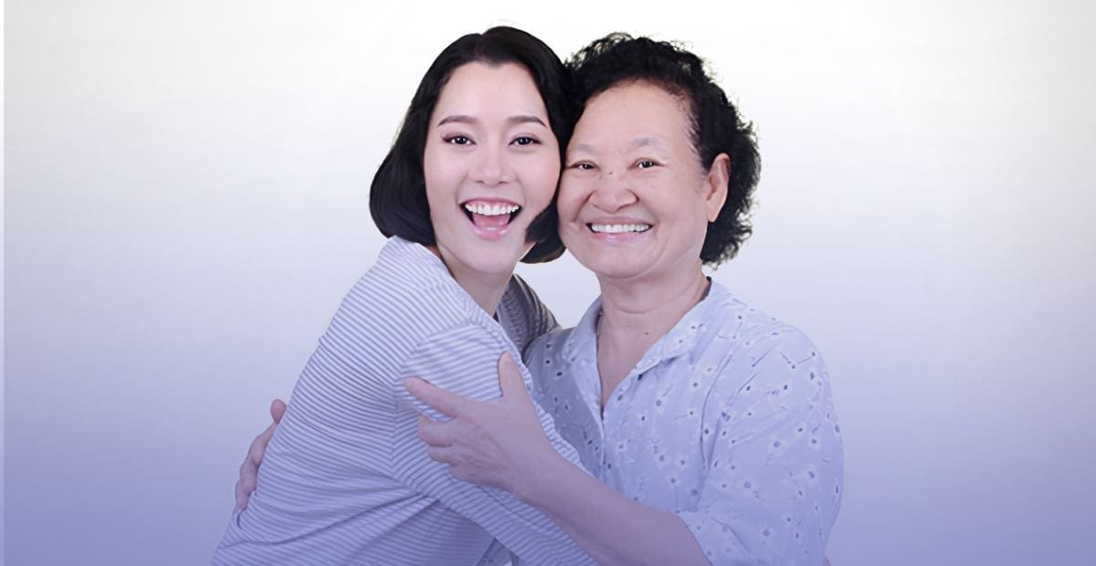 Two women smiling and hugging happily against a light background.