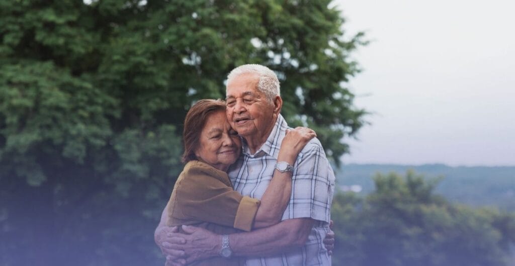An older couple embracing warmly outdoors, representing dignity and support in senior elder care.