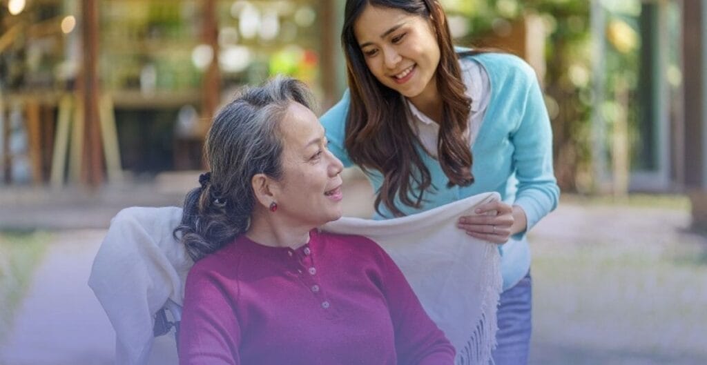 A smiling caregiver gently placing a blanket over an older adult seated outdoors, representing comprehensive care and protection for loved ones with incontinence.